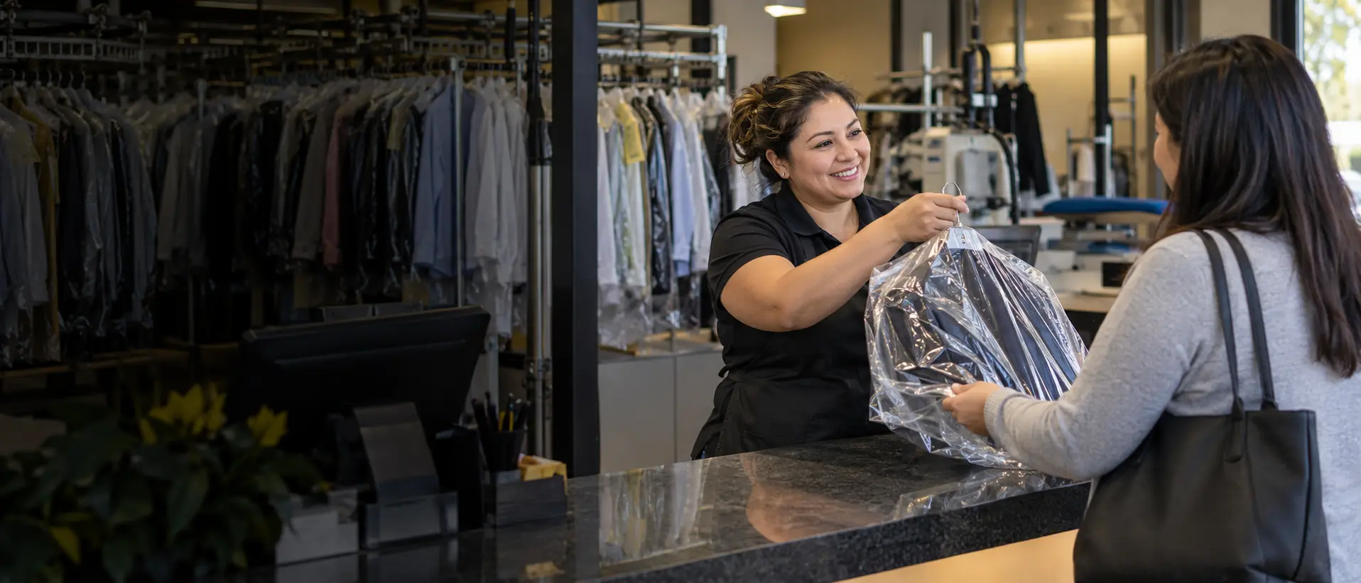 A dry-cleaning employee returning a freshly cleaned garment to a customer
