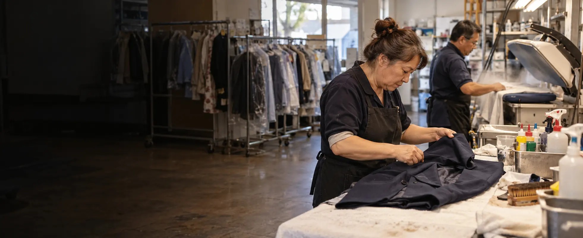 A neighborhood dry-cleaning team inspecting and pressing garments